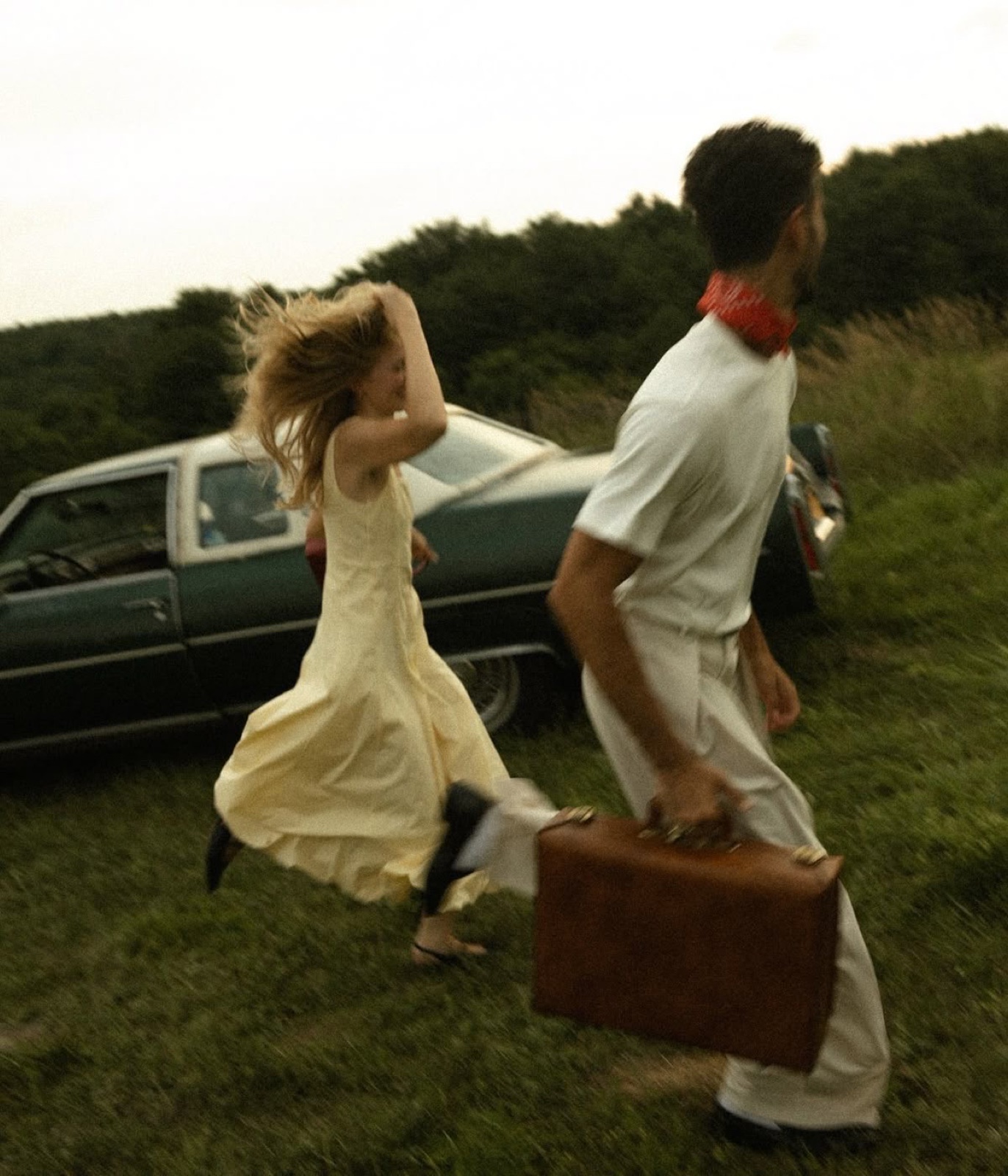 Couple running across a hillside with a suitcase