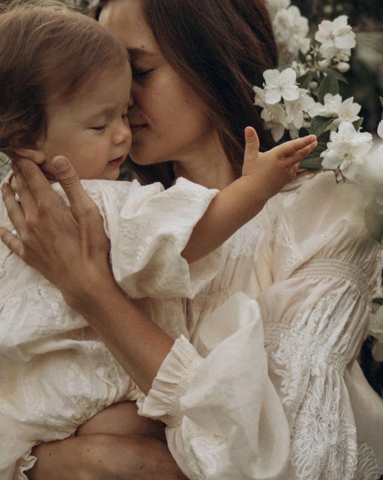 Mother holding her toddler surrounded by white flowers